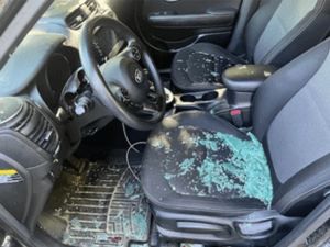 Driver and passenger seat of a Kia car with gray interior and shattered glass on the seats after a crash.